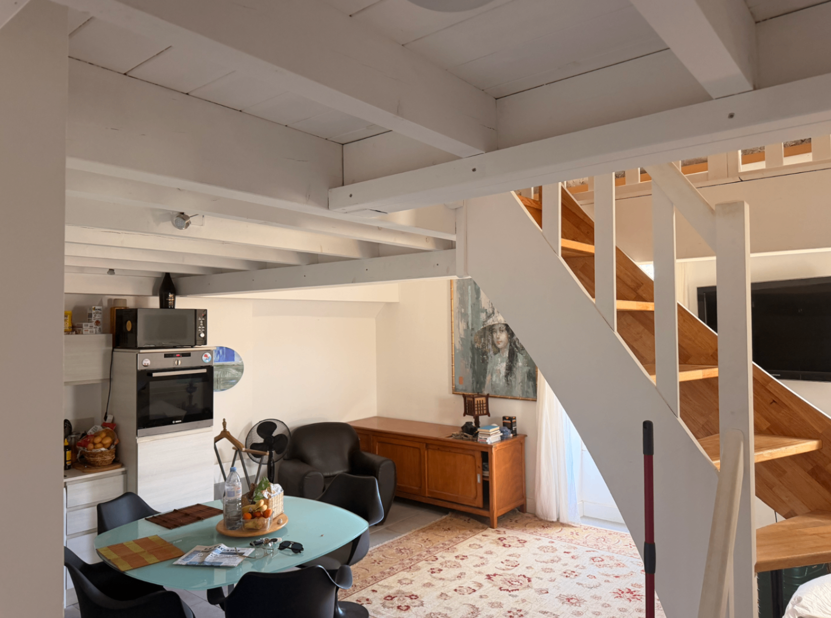 Living and dining area with exposed white beams and vintage credenza