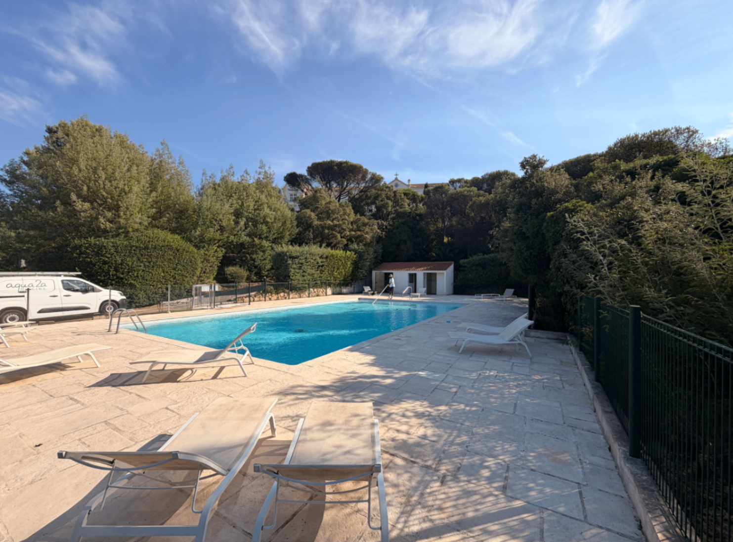 Wide pool terrace with loungers and the residence above the trees